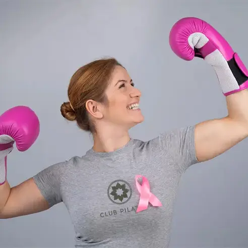 Mujer con guantes de boxeo y lazo rosa en Club Pilates Indautxu Bilbao, símbolo de fuerza en la lucha contra el cáncer de mama.
